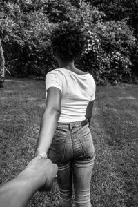 greyscale photography of woman walking with hand at the back holding other hand